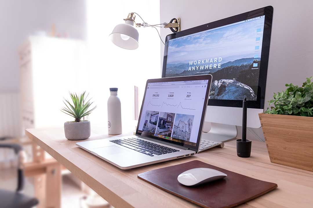 Laptop und Bildschirm an modernem Arbeitsplatz mit dem Schriftzug „Work hard anywhere“ – Symbol für berufliche Veränderung und neue Chancen für Medienprofis.